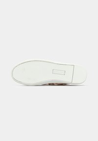 Πάτος λευκού αθλητικού παπουτσιού με λαστιχένια σόλα που έχει μοτίβο ψαροκόκαλο και το κείμενο «LAUREN» ανάγλυφο κοντά στη φτέρνα.