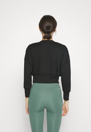 Svart kort sweatshirt med långa ärmar, elastisk nederdel, kombinerad med gröna högmidjade leggings. Slät tygtextur, minimalistisk design.