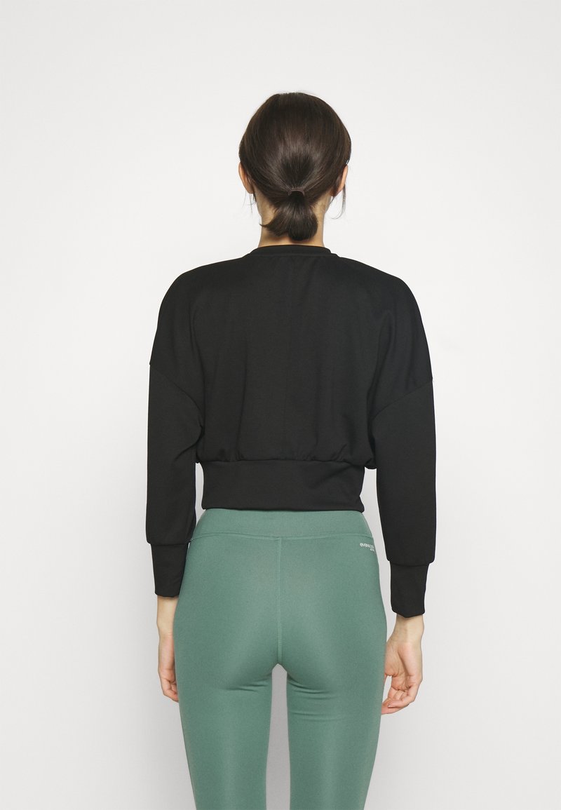 Sudadera negra corta con mangas largas, con dobladillo elástico, combinada con leggings verdes de cintura alta. Textura de tela suave, diseño minimalista.