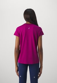 Camiseta deportiva de manga corta en un vibrante magenta, con cuello redondo y un sutil logo en la parte posterior, hecha de un tejido transpirable.