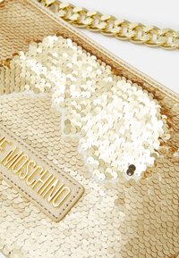Goldene Pailletten-Clutch mit einem goldenen Kettenriemen und einem MOSCHINO-Label in goldener Schrift, das auf dem Stoff an die Tasche genäht ist.
