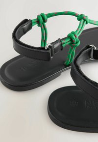 Zwarte leren sandalen met groene en roze patroonkoordbanden, platte zool en metalen sieraccenten.