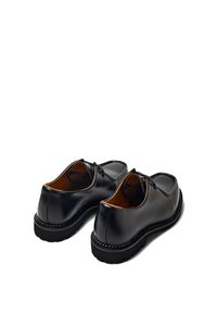 Zapatos de cuero negro con textura suave, punta redonda y diseño de cordones. Detalles de costura notables en la suela y forro interior marrón.