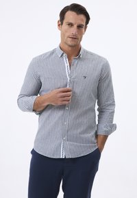 Camisa de manga larga a rayas en azul y blanco, con cuello de botones, que presenta un pequeño logo en el pecho, fabricada con un tejido ligero.