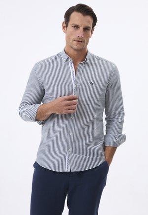 Camisa de manga larga a rayas en azul y blanco, con cuello de botones, que presenta un pequeño logo en el pecho, fabricada con un tejido ligero.
