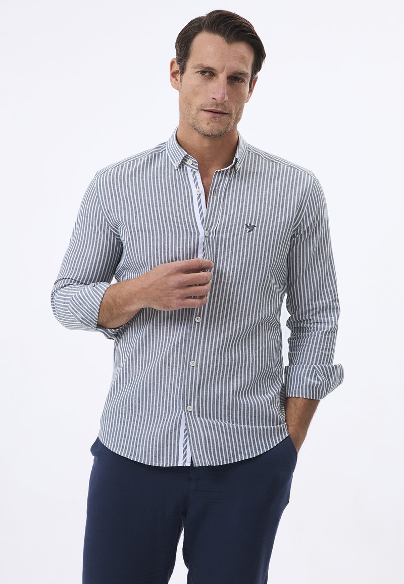 Camisa de manga larga a rayas en azul y blanco, con cuello de botones, que presenta un pequeño logo en el pecho, fabricada con un tejido ligero.