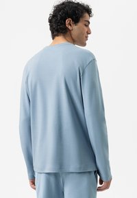 Himmelblaues, langärmliges Hemd aus weichem Stoff mit lockerer Passform, Rundhalsausschnitt und gestickten Saumdetails, kombiniert mit passenden Hosen.