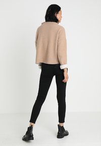 Suéter corto beige con cuello alto, combinado con Jeans ajustados negros y botines negros, que presentan una textura suave y un diseño ceñido.
