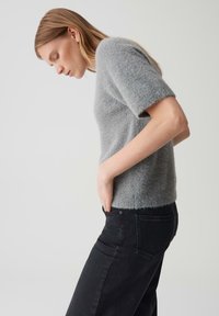 Grijze gebreide trui met korte mouwen, zachte textuur en geribde zoom, gecombineerd met hoge zwarte jeans, gezien vanuit de zijaanzicht.