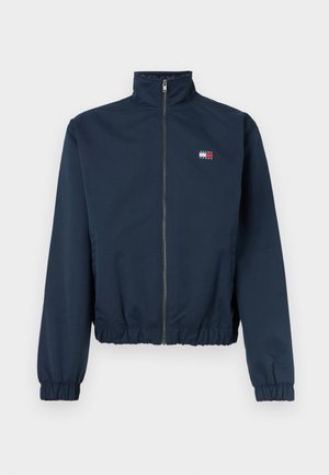 Námornícky modrá bunda na zips s elastickými manžetami a lemom, vysokým golierom a malým logom Tommy Jeans na ľavej strane hrude.