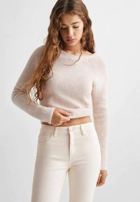 Maglione a coste rosa chiaro con maniche lunghe, design aderente, realizzato in una texture morbida, abbinato a jeans crema a vita alta.