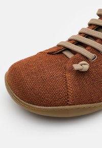 Scarpa in tessuto intrecciato marrone con punta arrotondata, lacci beige e suola in gomma. Presenta dettagli cuciti e una superficie texturizzata.