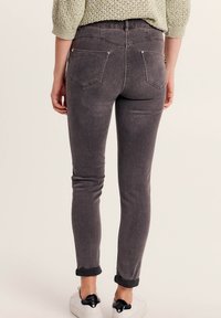 Jeans skinny grigi realizzati in denim, con vita bassa, cinque tasche e orli arrotolati, abbinati a sneakers bianche.