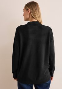 Maglione oversize nero con texture a coste sulle spalle e sul colletto; tessuto morbido; vestibilità ampia; maniche lunghe; orlo inferiore rifinito con coste.