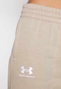 Bež dukserice s rebrastim strukom i bočnim džepovima. Ima bijeli Under Armour logo na gornjoj nozi. Mekani, teksturirani materijal.