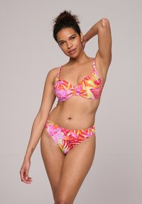 Kostium kąpielowy w kwiatowy wzór w żywych odcieniach różu, pomarańczy i zieleni. Górna część ma miseczki i regulowane ramiączka, a dół jest w średnim stylu.