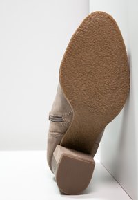 Bota de tobillo de ante marrón con suela de goma texturizada, tacón bajo y cierre de cremallera lateral para facilitar su uso.