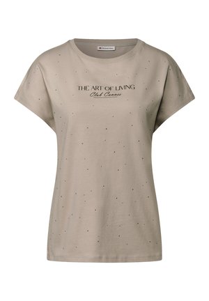 Camiseta de manga corta beige con cuello redondo, que presenta el texto negro "THE ART OF LIVING Club Cannes" y puntos negros dispersos como decoración.