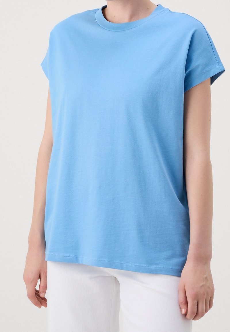 Ljusblå bomullströja med rund hals och korta ärmar. Något lös passform, slät textur och rak fåll. Bärs med vita byxor.