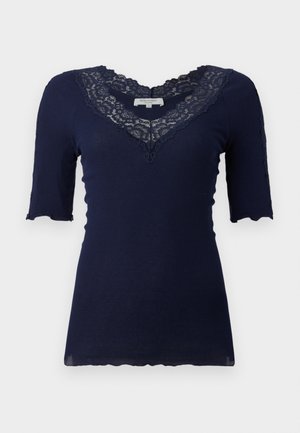 Tumedav sinine soonikkoes lühikeste varrukate ja sakilise äärisega. Omab pitsiga ääristatud V-kaelust ning pitsiaktsente varrukatel.