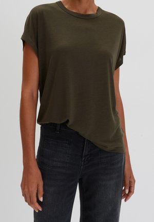 Oliwkowa koszulka z krótkim rękawem, okrągłym dekoltem, luźnym krojem i gładkim materiałem, w połączeniu z ciemnymi dżinsami z tylnymi kieszeniami.
