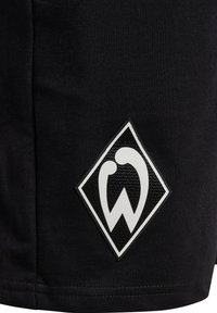 Svarta sportshorts med en strukturerad svart och vit emblem i diamantform på sidan. Slät tyg, enkel design.