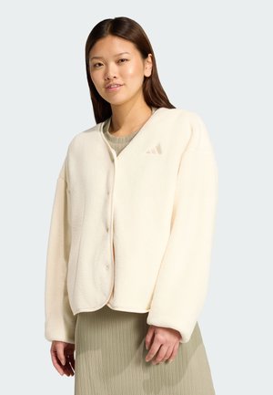 Vaaleanbeige fleece-takki, jossa on V-pääntie, nappikiinnitys ja ribbireunat. Takissa on hillitty logo rinnassa ja rento malli.