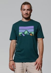 T-shirt en coton bleu-vert avec des manches courtes, présentant un graphique de montagne en violet, vert et orange. Encolure ronde, texture douce.