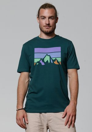 Teal katoenen T-shirt met korte mouwen, met een bergafbeelding in paars, groen en oranje. Ronde halslijn, zachte textuur.