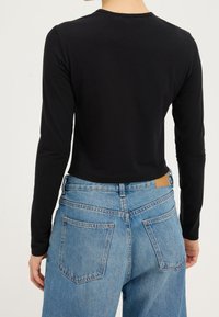 Top corto negro de manga larga con cuello redondo, combinado con unos pantalones vaqueros de tiro alto en azul con bolsillos parche y un lavado claro.