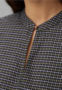 Overhemd met kraag in een donkergroen en blauw geruit patroon, voorzien van een kleine keyhole-opening en een ronde koperkleurige knoopsluiting.