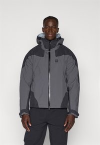 Chaqueta impermeable gris con cierre de cremallera, capucha ajustable y paneles de acento en un tono más oscuro en los hombros y las mangas.
