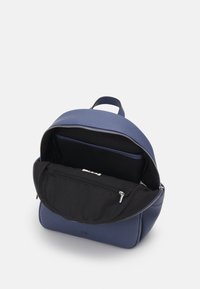 Zaino in pelle blu con forma arrotondata, caratterizzato da una parte superiore con zip e una tasca interna in tessuto nero. Hardware della cerniera e manico ad anello degni di nota.