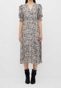 Robe midi fleurie avec manches bouffantes en beige et marine, dotée d'un col en V et d'un tissu fluide. Associée à des bottines souples bleu marine.
