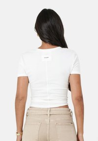 Witte aansluitende t-shirt met korte mouwen, met een naad op de rug en een label bij de halslijn. Glad textuur van de stof, gecombineerd met beige hoge taille broek.
