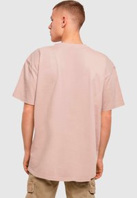 Světle růžové oversized tričko s krátkými rukávy, kulatým výstřihem a hladkým bavlněným materiálem. Viditelné švy na spodním lemu.