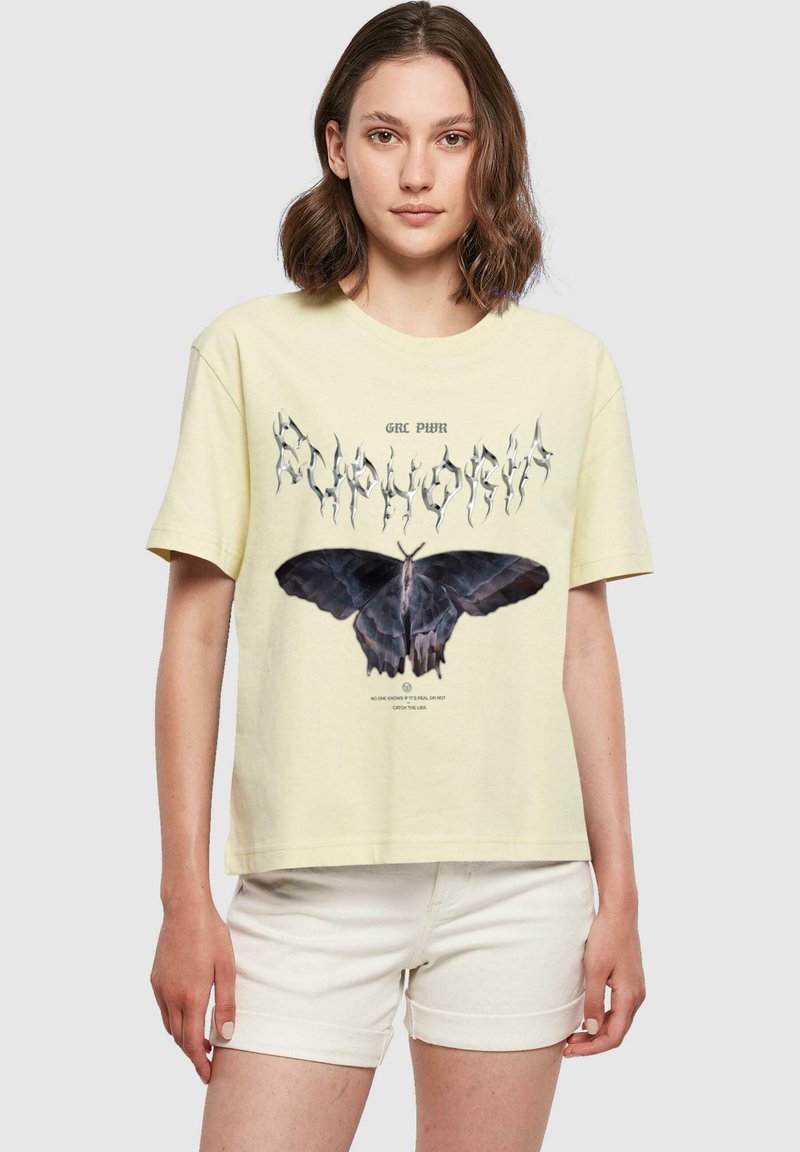 Gul bomullströja med en svart fjärilsgrafik och stiliserad text ovanför, kombinerad med ljusa shorts. Korta ärmar, avslappnad passform.