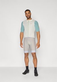 Vêtements de sport pour hommes comprenant un maillot à manches courtes gris clair avec des manches turquoise, une fermeture éclair à l'avant et un short de cyclisme gris clair assorti.