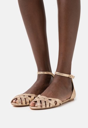 Goldene flache Sandalen mit einem geflochtenen Riemendesign, offener Zehenpartie und Knöchelriemen. Glatte Textur und niedriges Profil.
