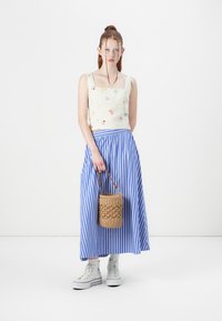 Top de vară alb cu flori, fustă maxi în dungi albastre și albe, adidași albi, cu o geantă împletită maro. Ținută de vară casual cu modele distincte.