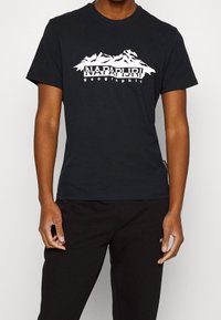 Mustaa puuvillapaitaa, jossa on valkoinen vuoristografiikka ja "Napapijri geographic" -teksti. Pyöreä kaula-aukko, lyhyet hihat ja pehmeä tekstuuri.