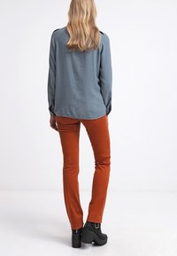 Blusa de manga larga, azul claro, con un corte holgado, combinada con pantalones ajustados de color óxido. Botas de plataforma negras destacadas. Texturas suaves visibles.