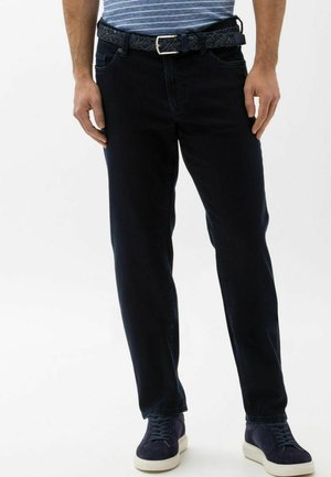 Dunkelblaue Jeans mit geradem Bein, ausgestattet mit einem geflochtenen schwarzen Gürtel, getragen mit marineblauen Sneakern und einem blau gestreiften Oberteil.