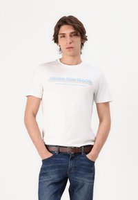 Valkoinen puuvillapaita, jossa sininen teksti "DENIM TOM TAILOR" rintamalla. Yhdistetty tummansinisiin farkkuihin ja ruskeaan vyöhön.