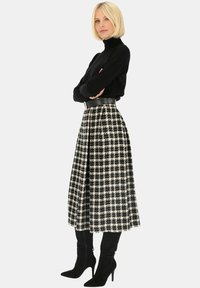 Czarny sweter z golfem zestawiony z midi spódnicą w czarno-białą kratę, z plisowanym wzorem i czarnym paskiem, dopełniony czarnymi, wysokimi botkami.