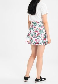 Mini falda floral en blanco, con patrones tropicales en verde y rosa. Combinada con una camiseta blanca básica y zapatillas negras.