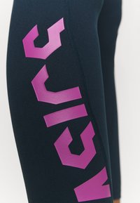 Närbild av svarta leggings med djärv lila geometrisk text som löper vertikalt längs yttre låret.
