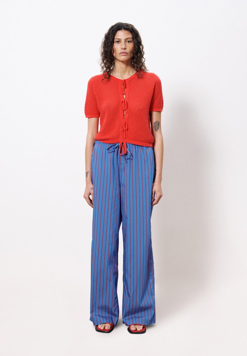 Haut à manches courtes en tricot rouge avec fermeture à nouer, associé à un pantalon large à rayures bleues et rouges, dotés d'une taille élastique et d'une texture lisse.