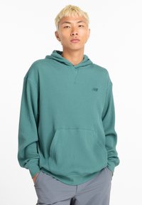 Sudadera con capucha de punto verde con un bolsillo frontal, corte relajado y capucha con cordón. Presenta un pequeño logo en el pecho. Hecha de tela texturizada.