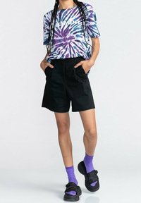 Tričeko s tie-dye vzorem v modré, fialové a bílé barvě s textem "ELEMENT", spárované s černými šortkami, fialovými ponožkami a černými sandály.